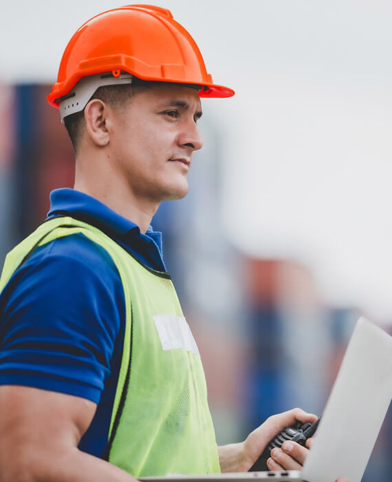 Customs management services coordinated by a Maverick Border Services collaborator who uses a radio and a laptop, while wearing a blue shirt, safety vest and orange helmet